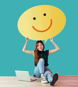 Girl holding happy face next to laptop